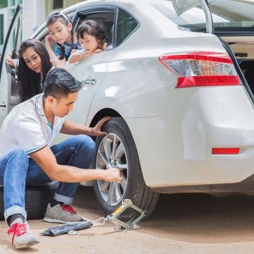 a man fixing car tyre and his family sitting in the car