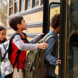 Niños subiendo a un autobús escolar amarillo, despidiéndose emocionados de sus padres y listos para un día de aprendizaje.