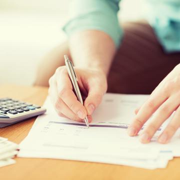 Un hombre que escribe en papel con bolígrafo y calculadora, calculando números y anotando información importante.