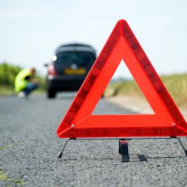 Una señal de advertencia de triángulo rojo a la costada de la carretera que indica peligros potenciales más adelante.