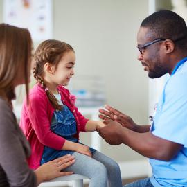 Un médico conversa amablemente con una niña, brindándole orientación y apoyo médico.