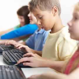 Niños sentados en un pupitre con ordenadores, participando en el aprendizaje y la exploración de recursos digitales.