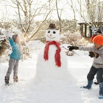 Un alegre grupo de niños jugando en la nieve, construyendo juntos un muñeco de nieve.