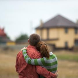 Una pareja abrazada frente a su casa, expresando amor y calidez en su relación.