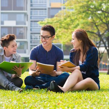 Estudiantes asiáticas estudiando al aire libre sobre césped con libros.