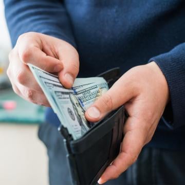 Un hombre sosteniendo una billetera llena de dinero, mostrando seguridad financiera y riqueza.