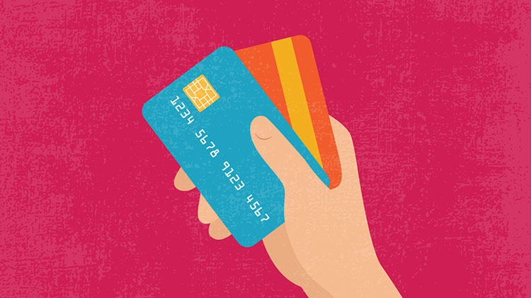 Una mano sosteniendo una tarjeta de crédito sobre un fondo rosa.