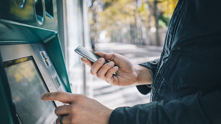 Una persona que usa un teléfono móvil en un cajero automático, lo que garantiza transacciones seguras y una banca conveniente.
