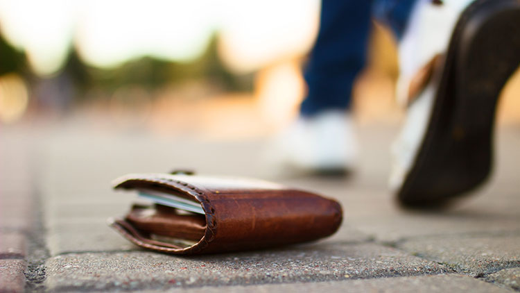 Una persona que camina por una acera de ladrillos, pasando junto a una billetera en el suelo.
