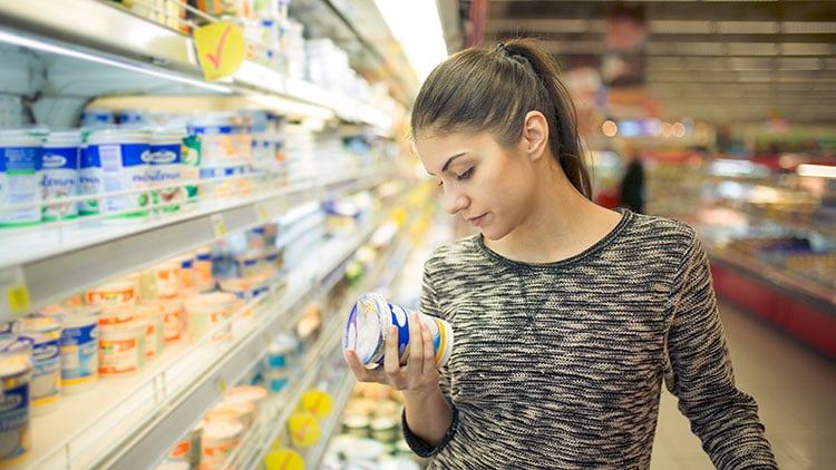 Una mujer examinando opciones de yogur en una tienda de comestibles.