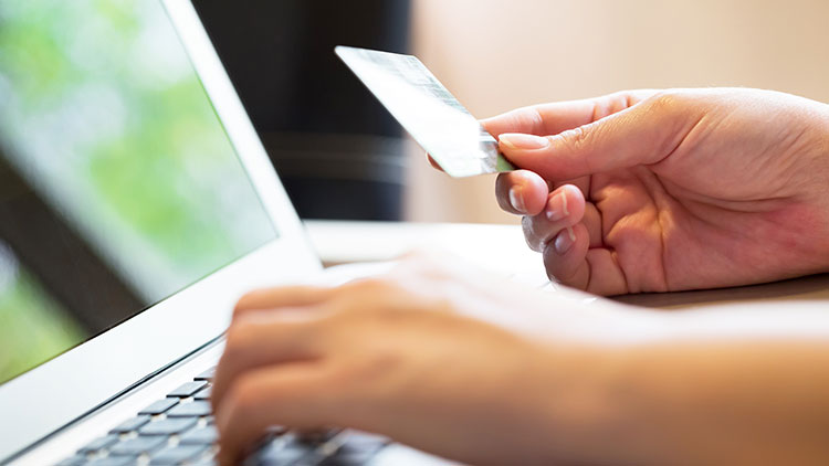 Una persona que realiza múltiples tareas con una computadora portátil y tiene una tarjeta de crédito para transacciones en línea.